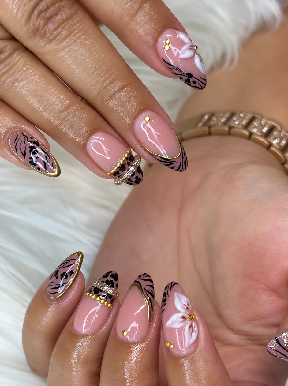 Almond nails with a nude base, leopard and zebra tips, gold details and white flowers
