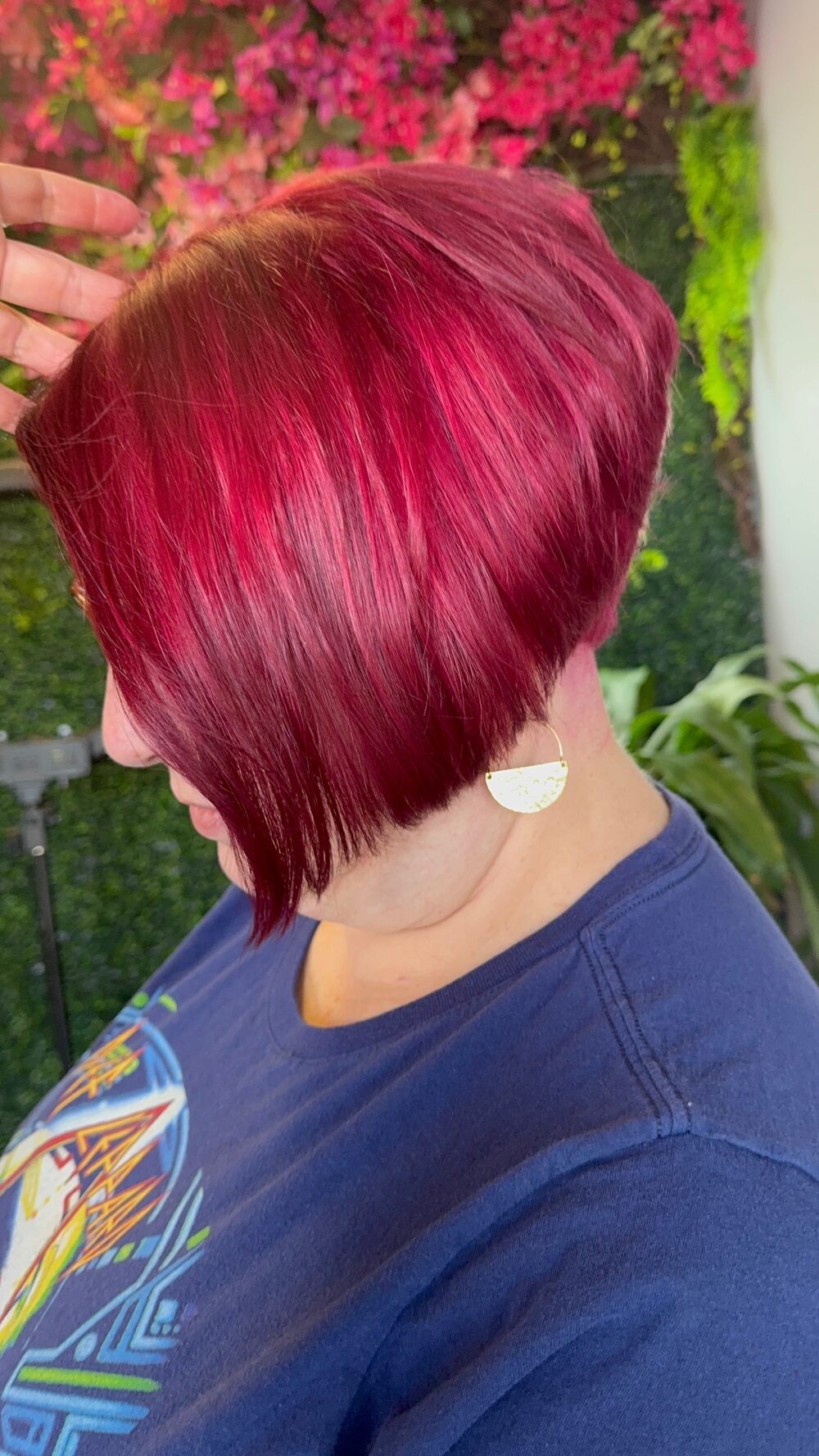 A sleek cherry red bob seen from the side in front of the flower wall